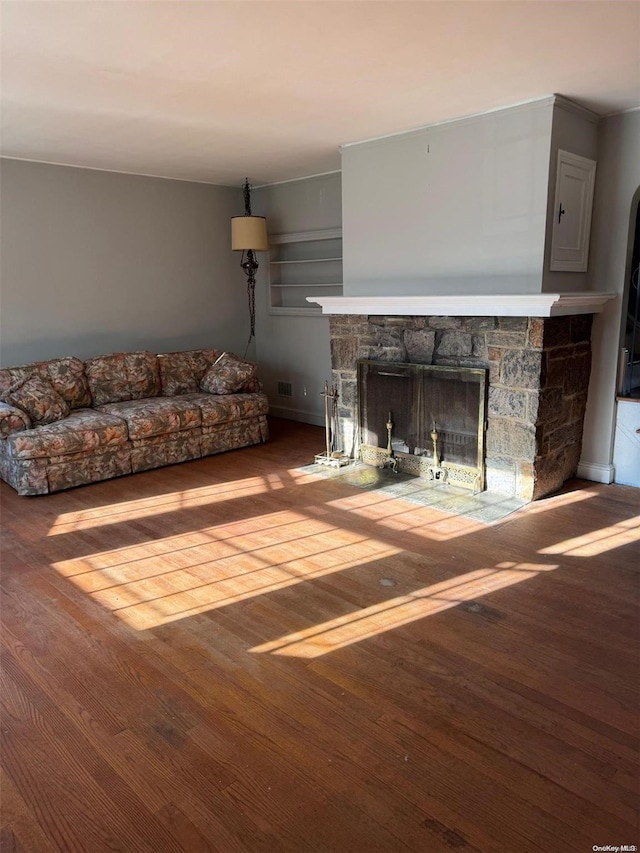 unfurnished living room with a stone fireplace, wood-type flooring, and crown molding