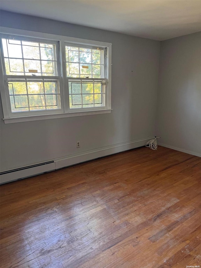 empty room with wood-type flooring and a baseboard heating unit