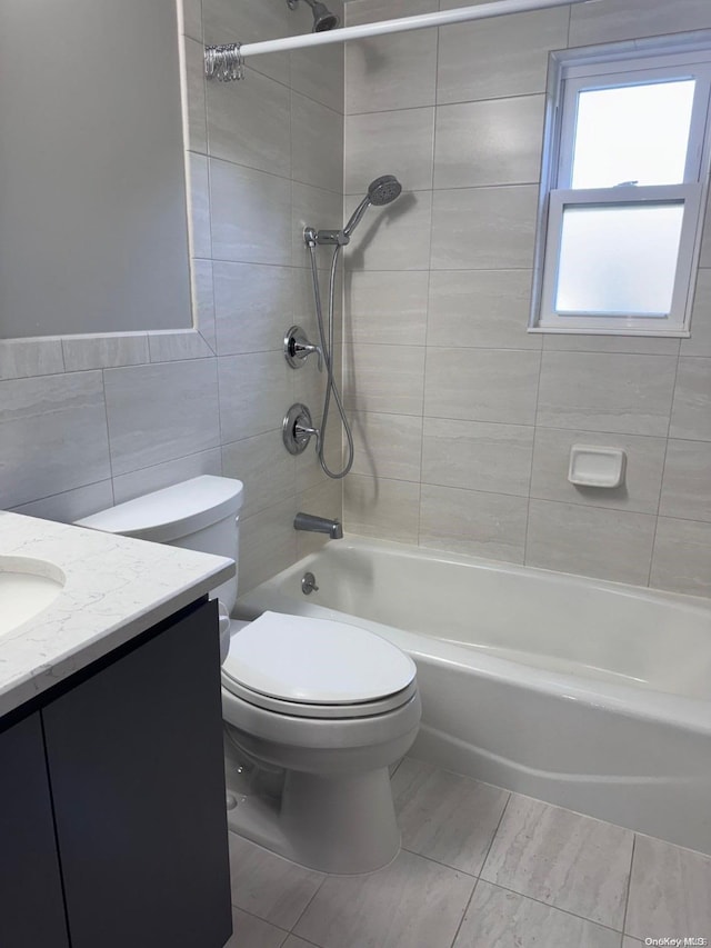 full bathroom featuring vanity, tile patterned floors, tiled shower / bath combo, toilet, and tile walls