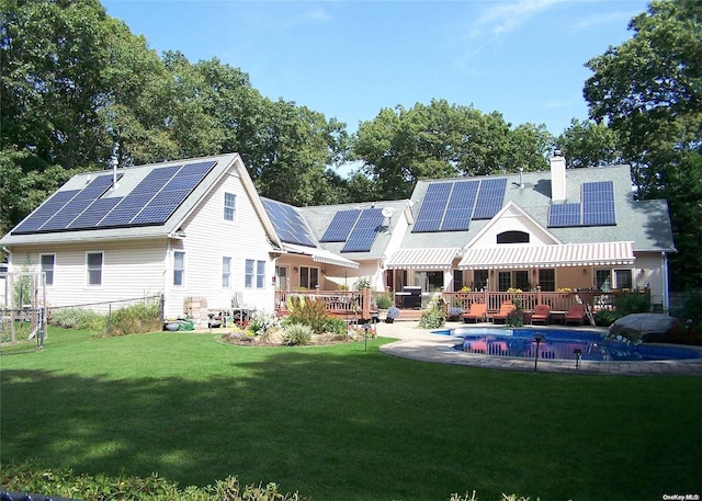 rear view of house featuring a lawn, a pool side deck, and solar panels