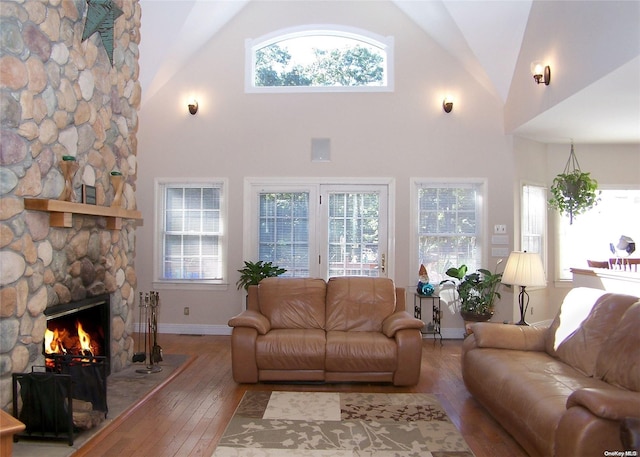 living room with hardwood / wood-style flooring, a stone fireplace, and high vaulted ceiling