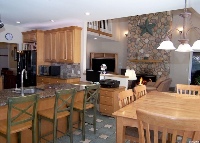 kitchen featuring sink, black fridge, pendant lighting, a fireplace, and a breakfast bar