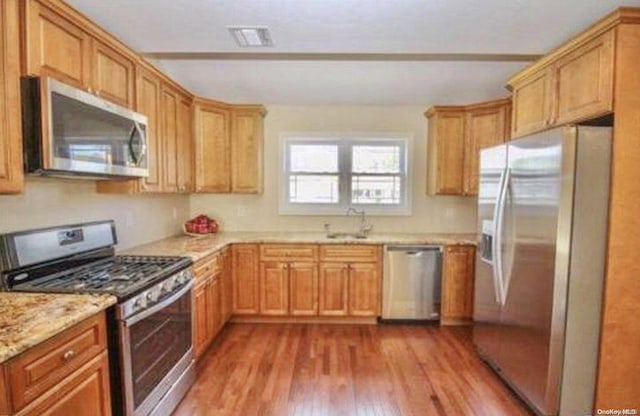 kitchen with light stone countertops, appliances with stainless steel finishes, wood-type flooring, and sink