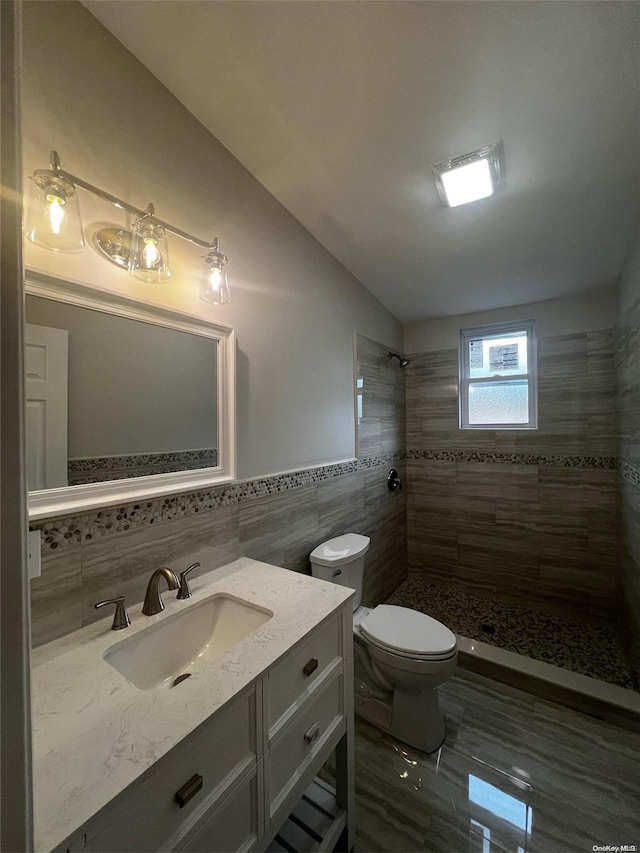 bathroom featuring vanity, toilet, tile walls, and a tile shower