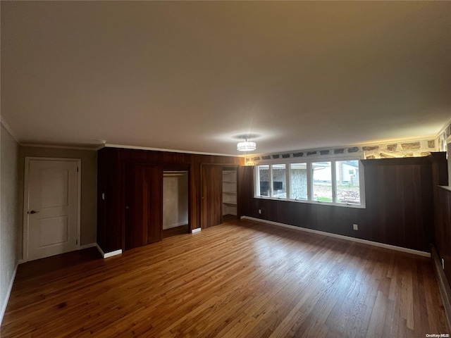 empty room with wood-type flooring, ornamental molding, and wooden walls