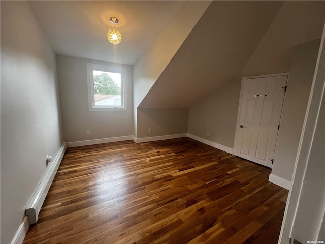 additional living space featuring dark wood-type flooring and vaulted ceiling