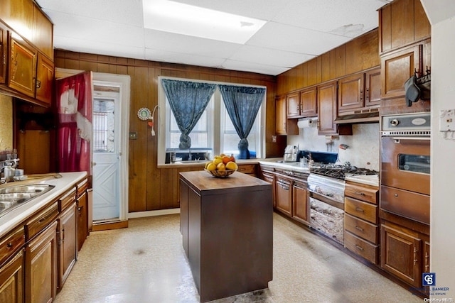 kitchen featuring a paneled ceiling, wooden walls, a kitchen island, and stainless steel appliances