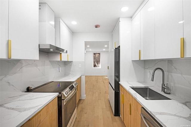 kitchen featuring light stone countertops, appliances with stainless steel finishes, wall chimney exhaust hood, white cabinets, and light hardwood / wood-style floors