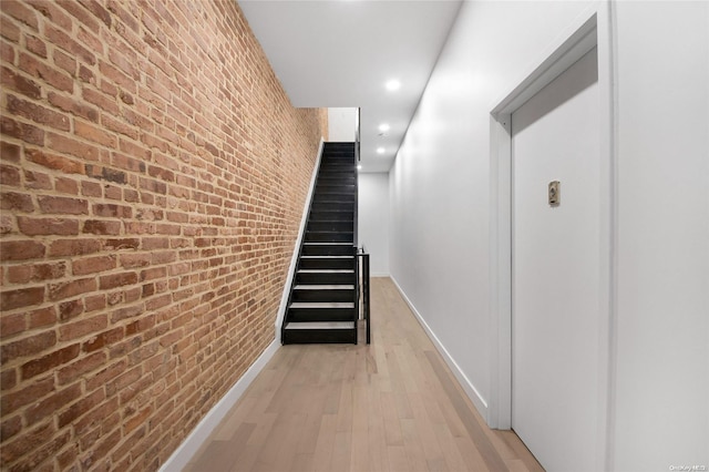 corridor featuring light wood-type flooring and brick wall