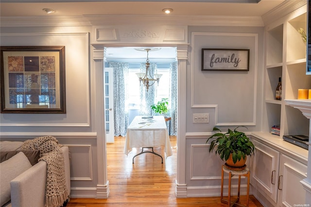 living area featuring built in features, light wood-type flooring, crown molding, and a chandelier