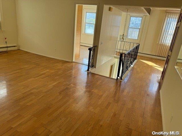 spare room with wood-type flooring, a wealth of natural light, and a baseboard heating unit