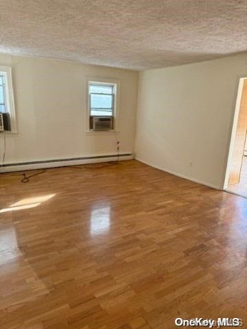 spare room with hardwood / wood-style floors, a textured ceiling, a baseboard radiator, and cooling unit