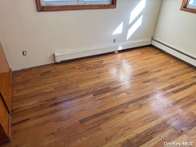 empty room featuring wood-type flooring and a baseboard radiator