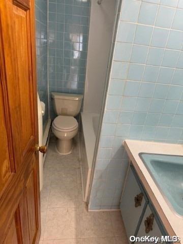 bathroom with toilet, tile patterned flooring, tile walls, and walk in shower