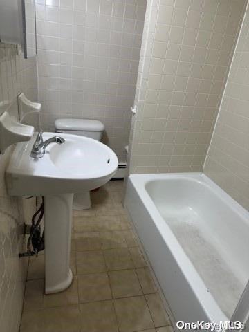 bathroom with tile patterned floors, tub / shower combination, toilet, and tile walls