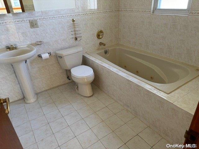 bathroom with tiled bath, toilet, and tile walls