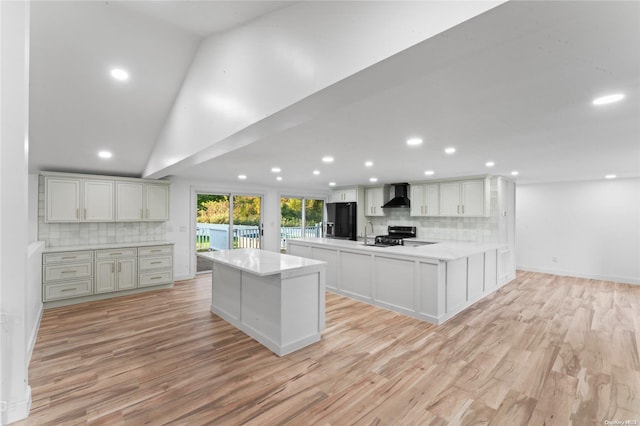 kitchen with white cabinetry, wall chimney range hood, backsplash, light hardwood / wood-style floors, and lofted ceiling