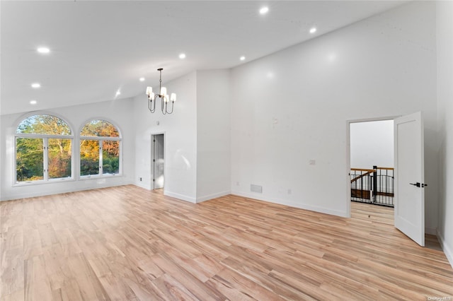 unfurnished living room featuring high vaulted ceiling, light hardwood / wood-style floors, and an inviting chandelier