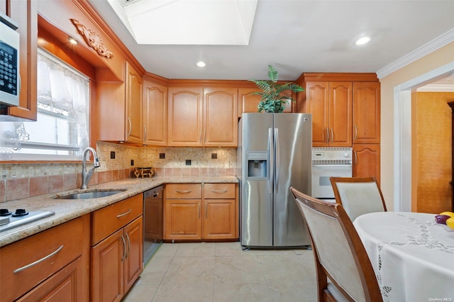 kitchen with a skylight, sink, light stone counters, crown molding, and appliances with stainless steel finishes