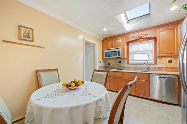 kitchen with sink, a skylight, ornamental molding, appliances with stainless steel finishes, and tasteful backsplash