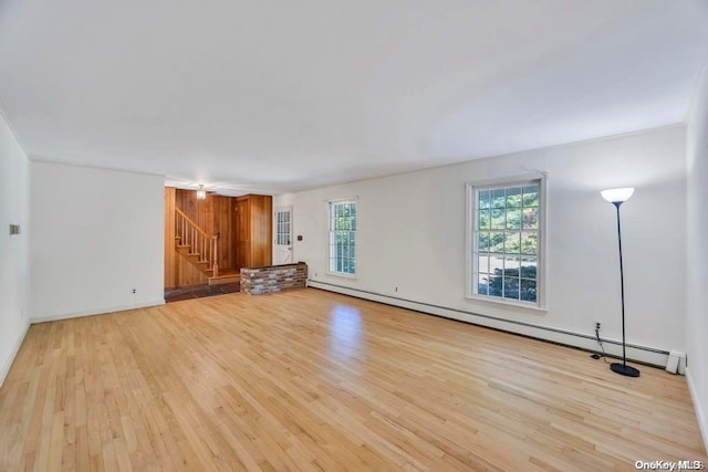 unfurnished living room with baseboard heating, a wealth of natural light, and light hardwood / wood-style floors