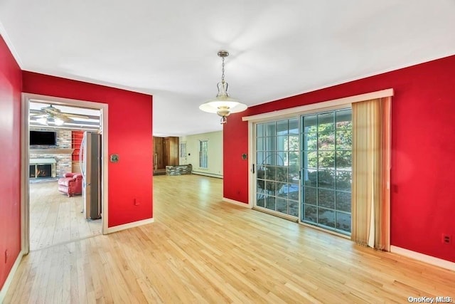 spare room featuring hardwood / wood-style flooring, ceiling fan, a fireplace, and a baseboard radiator