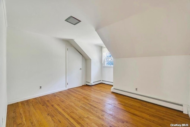 additional living space with light wood-type flooring, baseboard heating, and vaulted ceiling