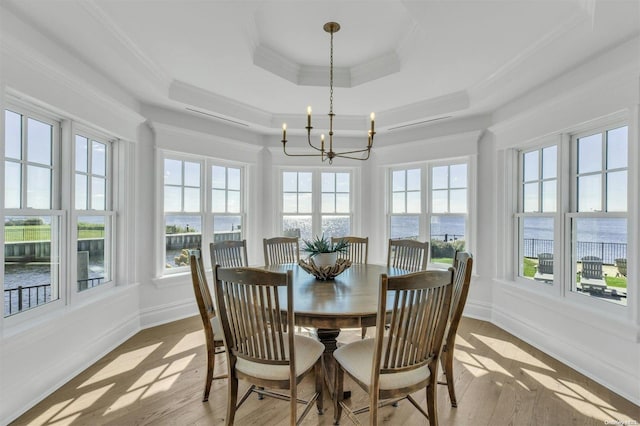 sunroom featuring a tray ceiling, a chandelier, a water view, and a healthy amount of sunlight