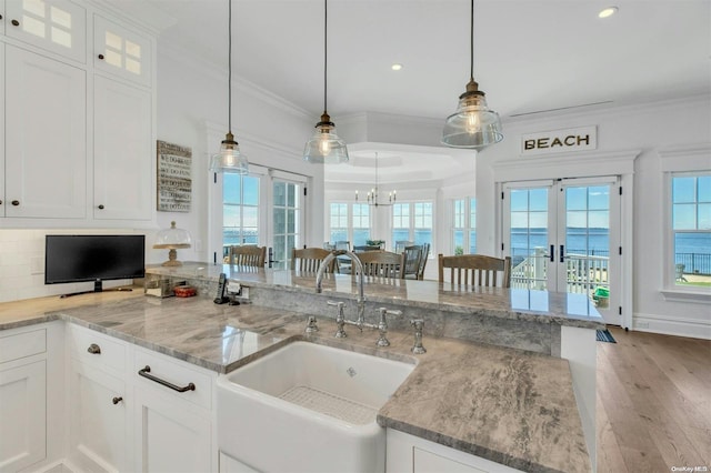 kitchen featuring french doors, sink, decorative light fixtures, a water view, and white cabinets