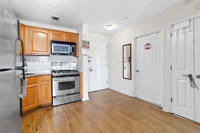 kitchen with tasteful backsplash, appliances with stainless steel finishes, and light hardwood / wood-style floors