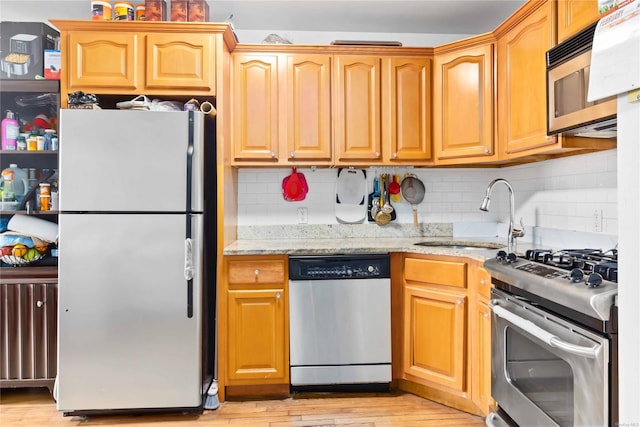 kitchen featuring light stone countertops, appliances with stainless steel finishes, sink, and light hardwood / wood-style flooring