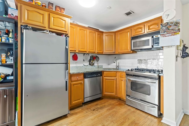 kitchen with appliances with stainless steel finishes, tasteful backsplash, sink, light stone countertops, and light hardwood / wood-style flooring