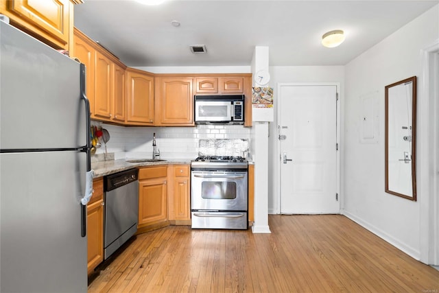 kitchen with sink, light hardwood / wood-style flooring, stainless steel appliances, tasteful backsplash, and light stone countertops