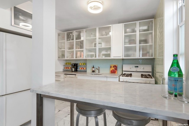 bar with light stone counters, white cabinetry, gas range gas stove, and sink