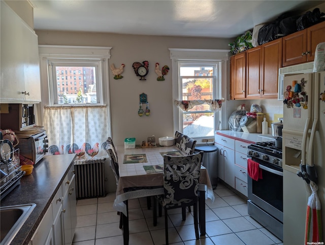 kitchen featuring sink, stainless steel gas range, white fridge with ice dispenser, light tile patterned floors, and radiator heating unit