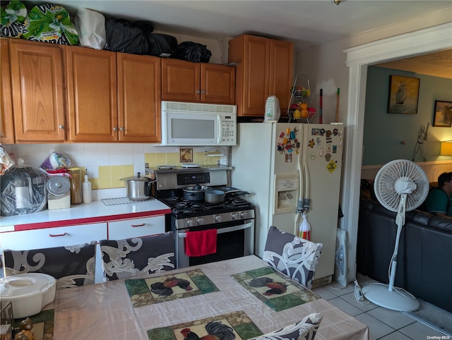 kitchen featuring backsplash, light tile patterned floors, and white appliances