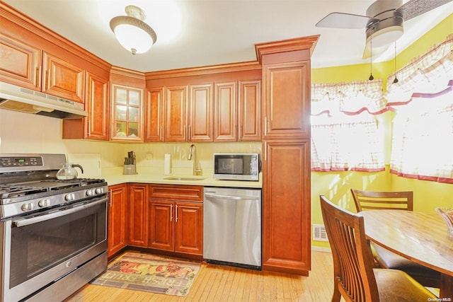 kitchen with appliances with stainless steel finishes, ventilation hood, ceiling fan, sink, and light hardwood / wood-style floors