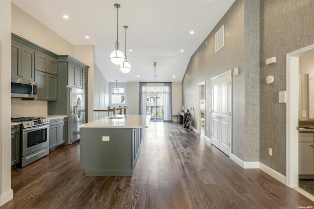 kitchen featuring hanging light fixtures, dark hardwood / wood-style flooring, a towering ceiling, a kitchen island with sink, and appliances with stainless steel finishes