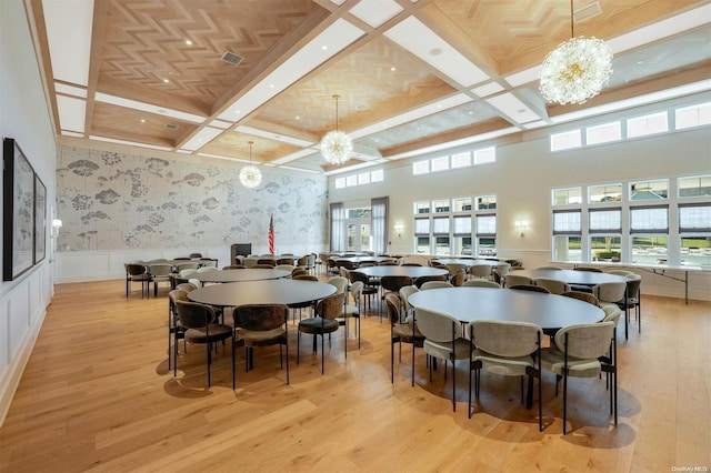 dining area with a towering ceiling, light hardwood / wood-style flooring, a notable chandelier, and coffered ceiling