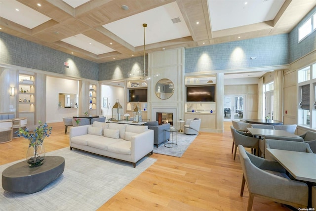 living room with coffered ceiling, a large fireplace, a towering ceiling, and light hardwood / wood-style flooring