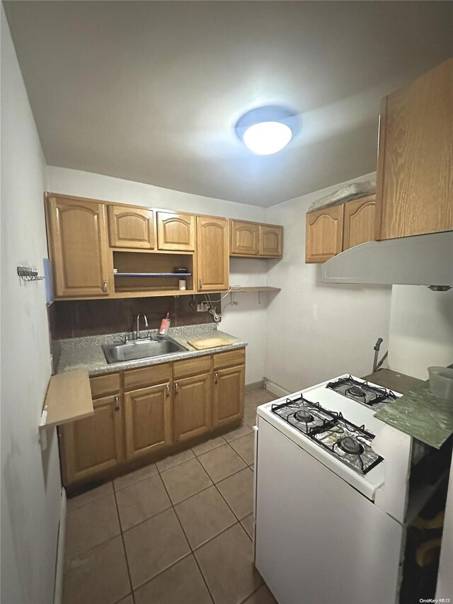 kitchen with tile patterned flooring, white range with gas stovetop, sink, and light brown cabinetry