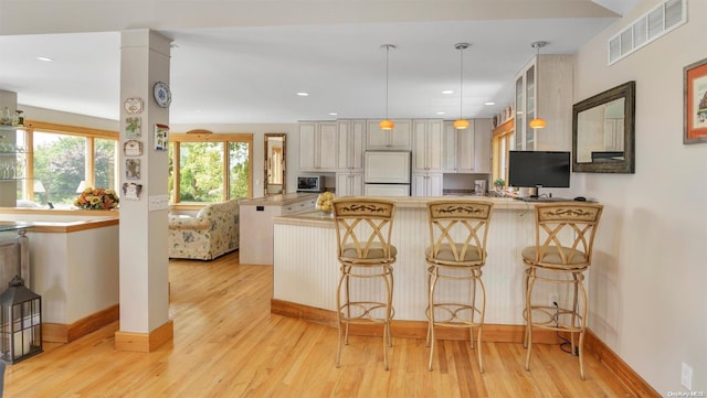 kitchen featuring a breakfast bar, light wood-type flooring, paneled built in refrigerator, kitchen peninsula, and pendant lighting