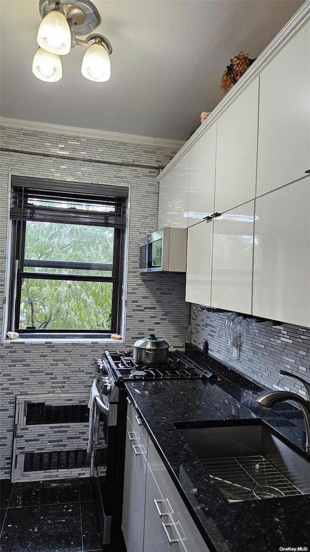 kitchen with white cabinetry, sink, stainless steel gas range oven, dark stone counters, and decorative backsplash