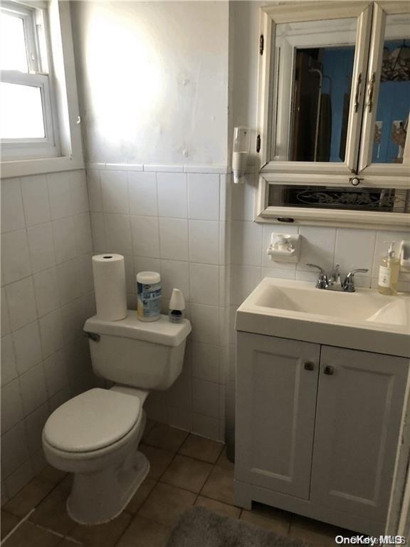 bathroom with tile patterned flooring, vanity, toilet, and tile walls