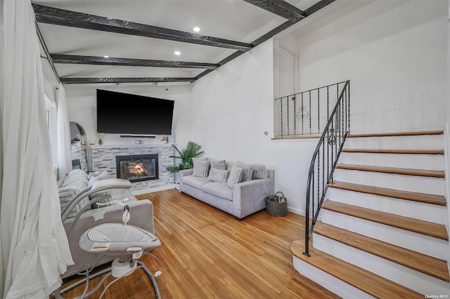 living room with beam ceiling, hardwood / wood-style flooring, and a stone fireplace