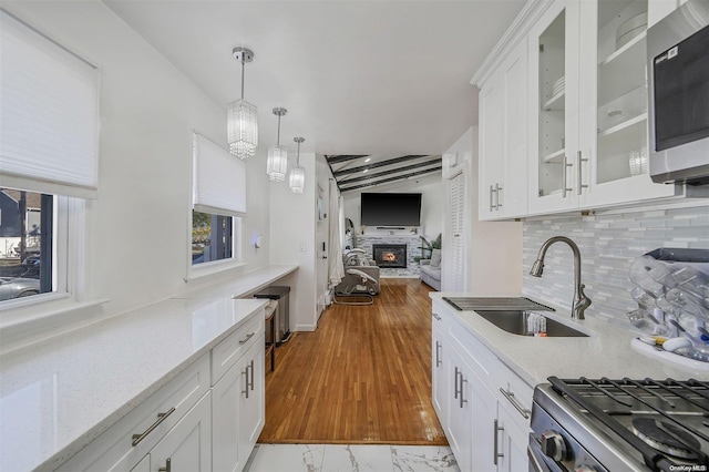 kitchen featuring sink, light stone counters, a fireplace, white cabinets, and appliances with stainless steel finishes