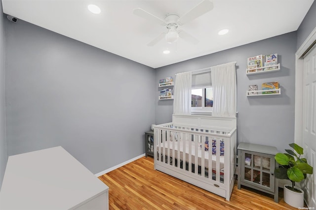 bedroom featuring hardwood / wood-style floors, a closet, a nursery area, and ceiling fan