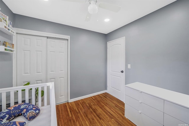 bedroom featuring a crib, wood-type flooring, a closet, and ceiling fan