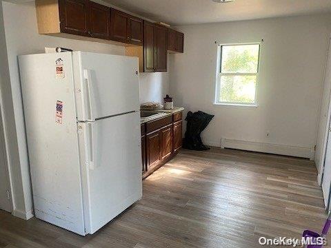 kitchen with dark brown cabinetry, white fridge, a baseboard radiator, and hardwood / wood-style flooring