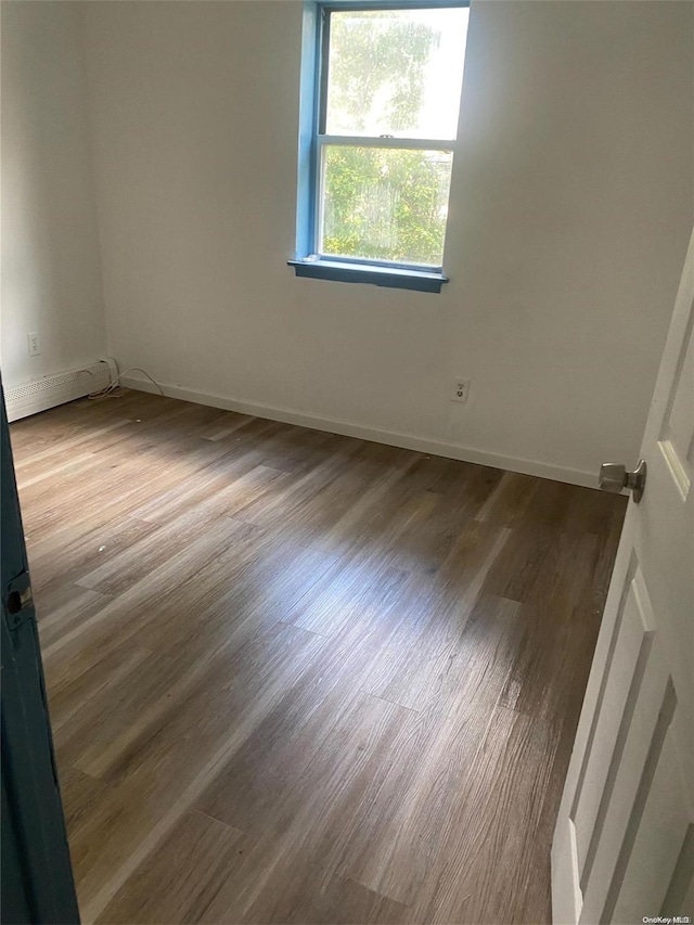 empty room with wood-type flooring and a baseboard heating unit